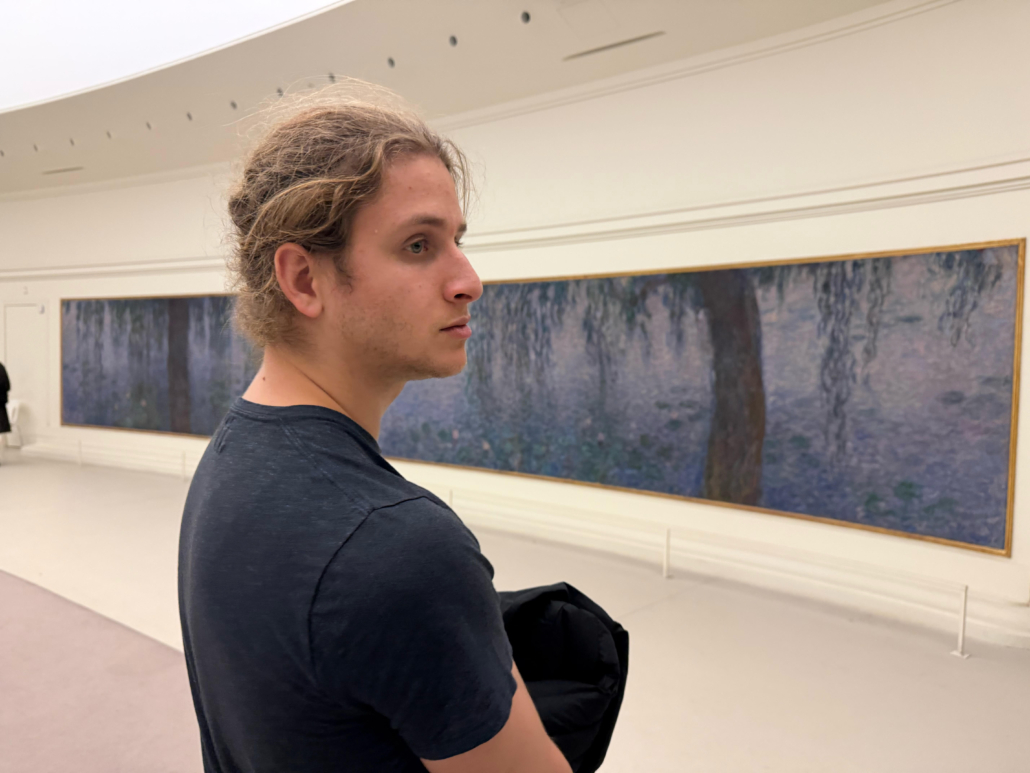 Right profile of blonde male student looking at art on white wall