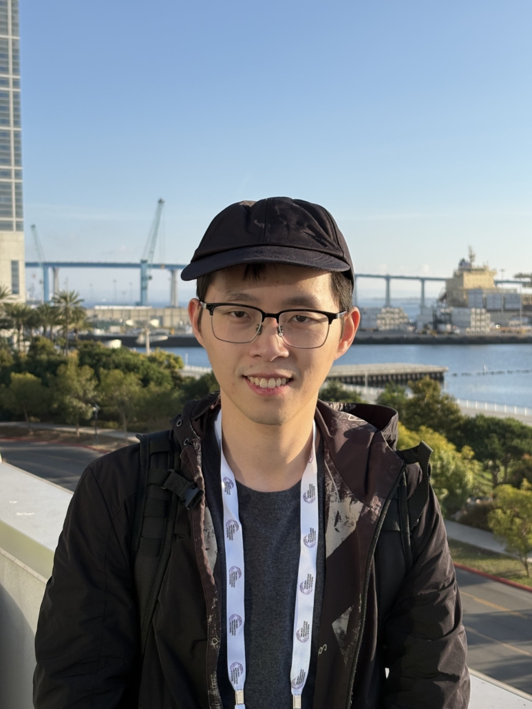 Man with glasses and hat standing in front of bridge and river